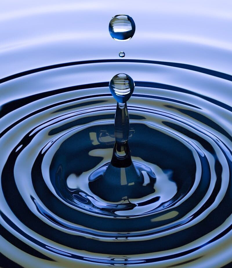 A stunning close-up of a water droplet creating ripples on a smooth water surface, capturing nature's simplicity.