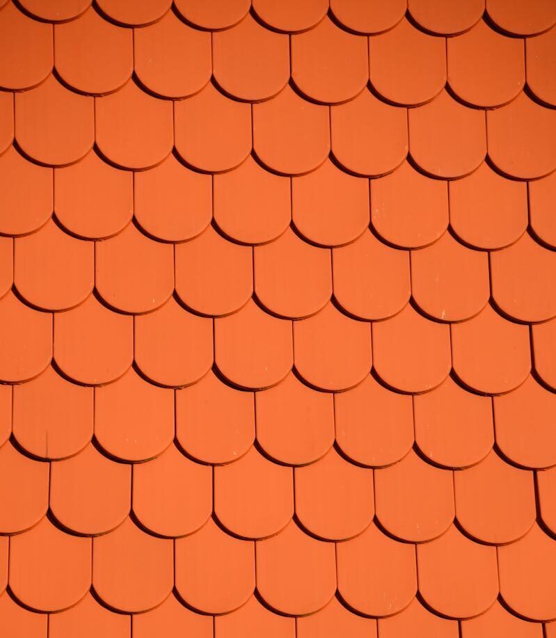 Bright orange roof tiles arranged in a seamless repetitive pattern, perfect for backgrounds and designs.